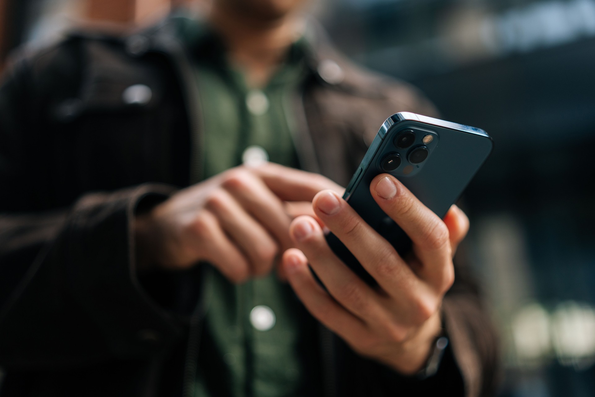 Adult man holding and using smartphone standing on city street, browsing internet, checking social media, using mobile application.